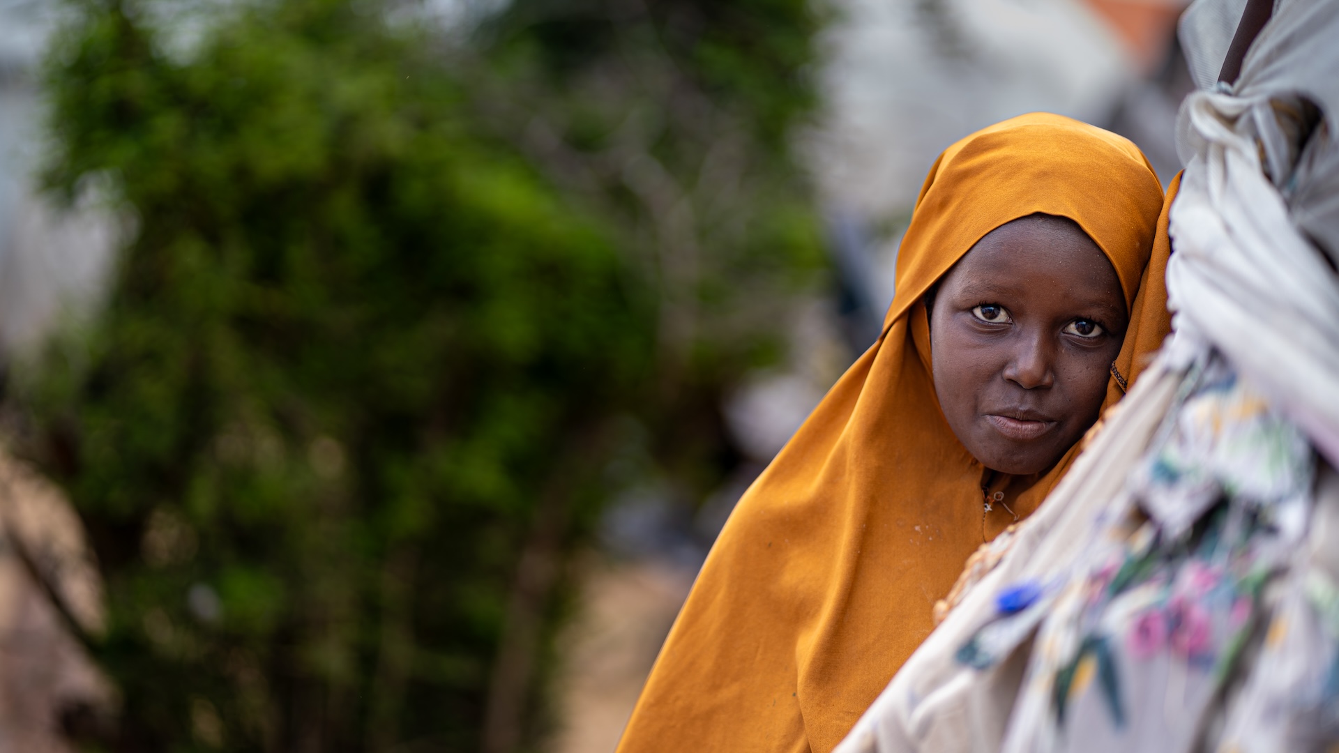 A young girl wearing an orange head covering looks towards the camera.