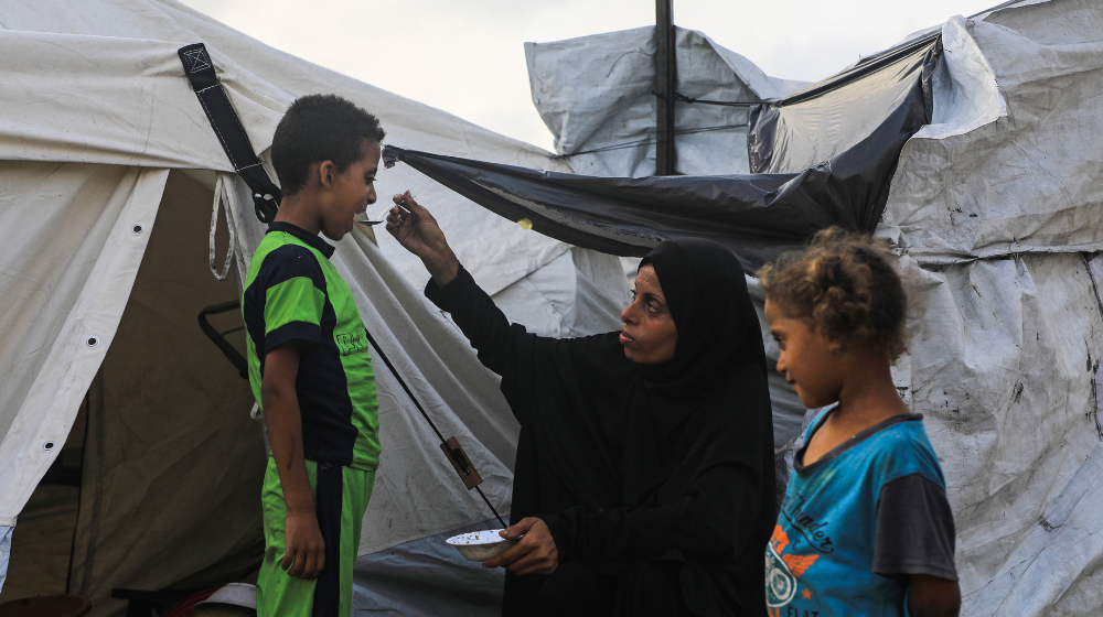 A woman feeds her children in front of their tent in a displacement camp