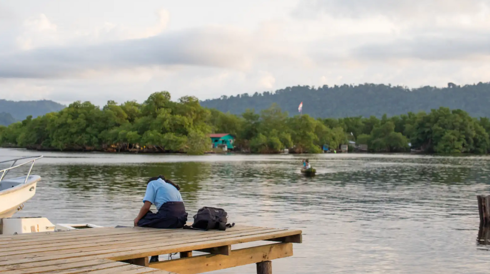 A girl leans over the side of a wooden deck by a lake in Bocas del Toro