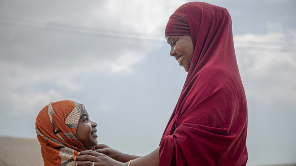 A mother adjusts her daughter’s hijab as they embrace and share a laugh