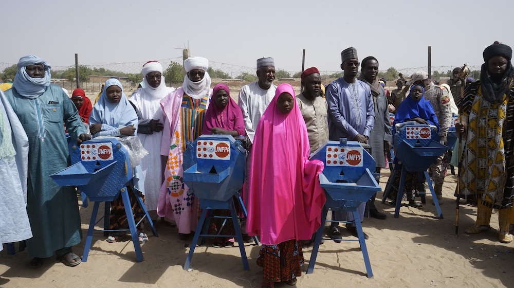 Teenage girls and men from Niger are standing next to grinding mills. 