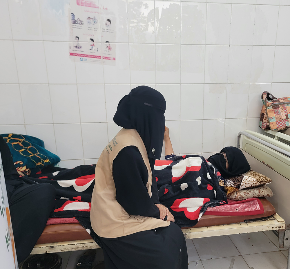 A woman in a UNFPA vest speaks to a woman lying on a hospital bed