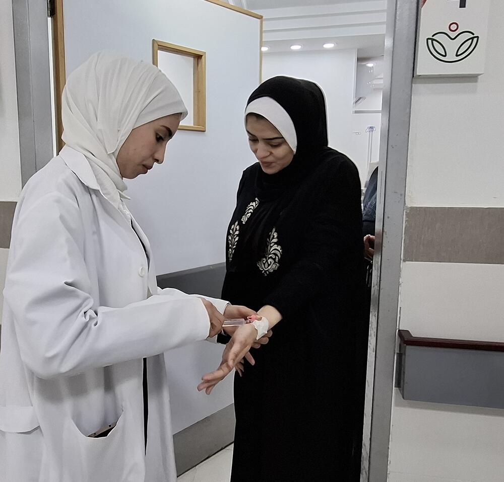 Une femme portant une blouse médicale blanche insère une seringue dans le poignet d’une patiente
