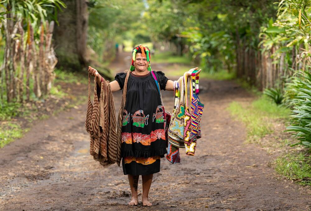 A smiling woman in a black dress is holding woven bags