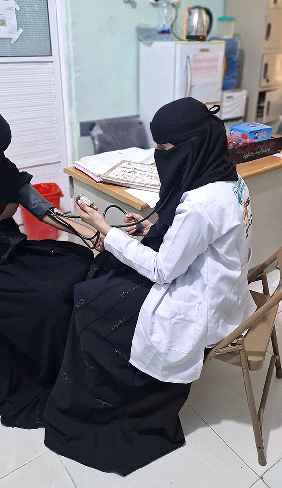  A female health worker takes the blood pressure of a woman seated in front of her