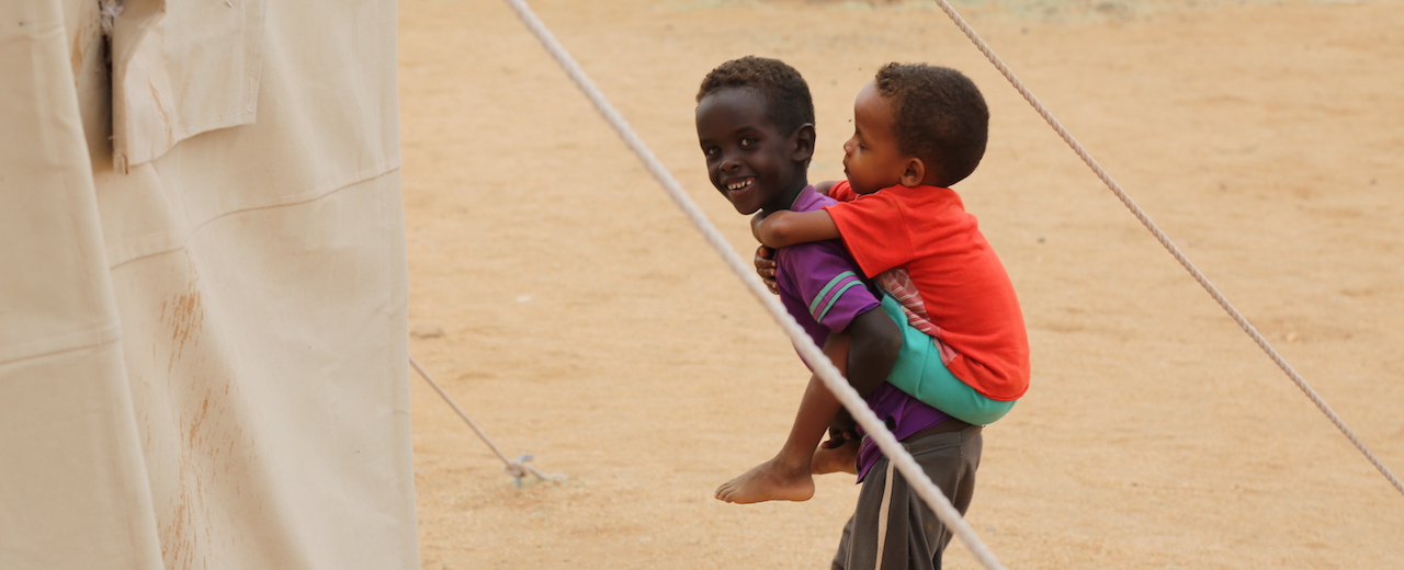A young boy smiles and holds a child on his back. 
