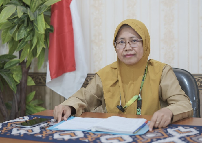 A woman in a yellow head covering sits behind a desk, with an open file in front of her
