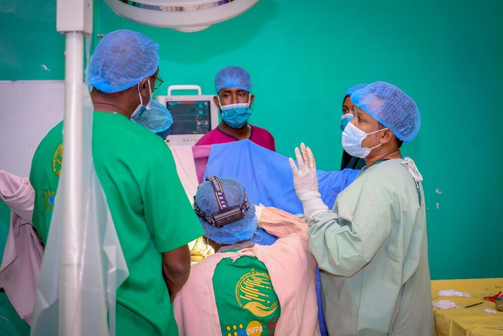 Health workers in scrubs, face masks and hairnets  gather around an operating table