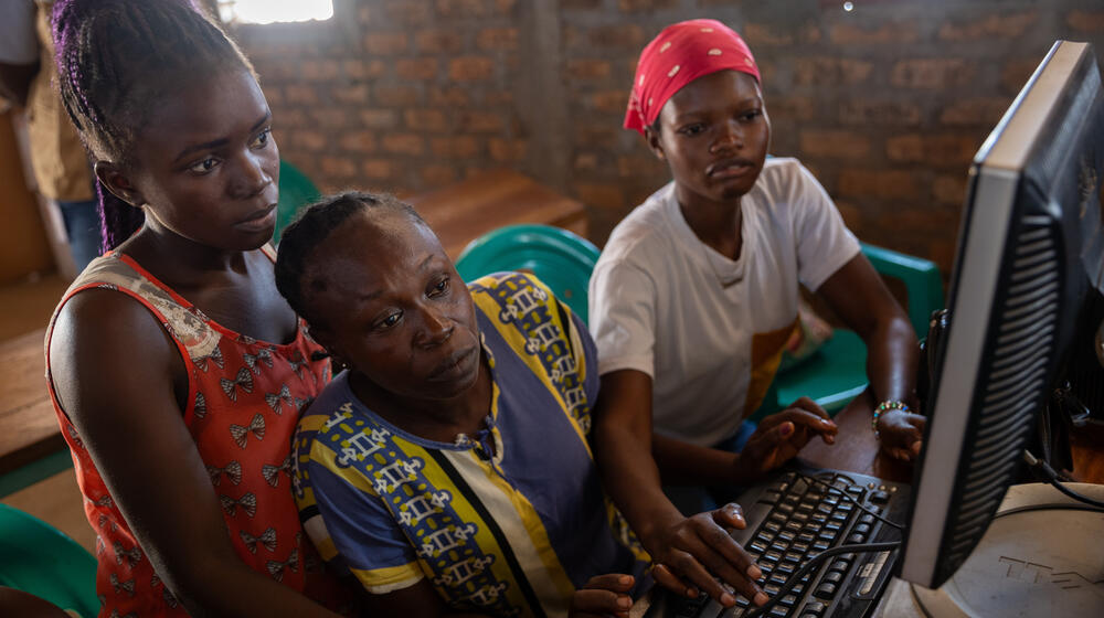 Three women look together at a computer screen.