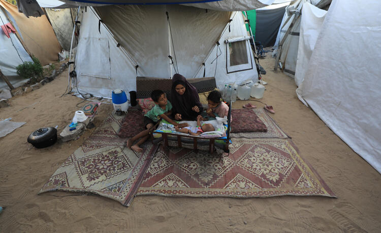 A woman sits with her three children beside their family tent in a displacement camp in western Gaza city; her baby is just two months old. Photo here © UNFPA Palestine/Hardy Skills 