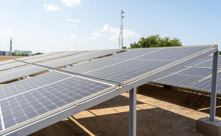 Solar panels line the rooftop of the maternity hospital. In the distance, a minaret can be seen.