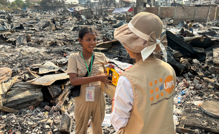  A young woman stands amid debris speaking to a woman in a hat and UNFPA vest