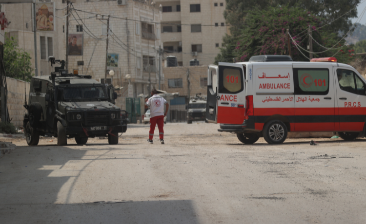 Un secouriste palestinien de la Croix-Rouge se tient sur la route devant une jeep de l’armée israélienne.