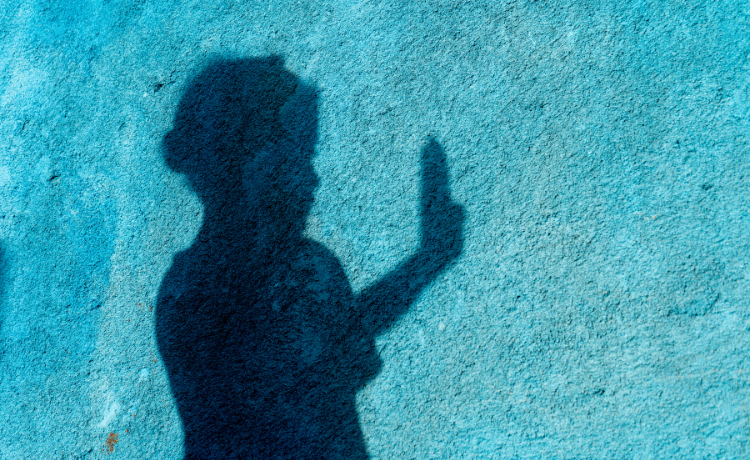 A girl in shadow holding up her hand against a bright blue wal