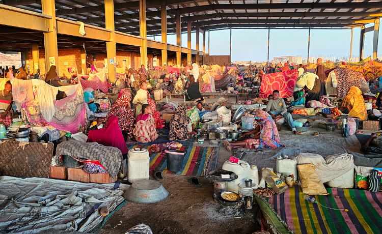 A large semi-covered space is full of people, blankets, tents and belongings