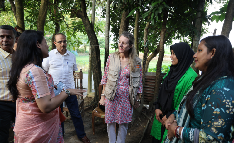 A woman in a UNFPA vest talks to a group of people in front of some trees.