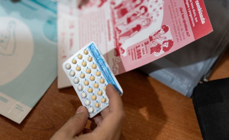 A hand holds a contraceptive birth control pill pack over a table filled with printed leaflets.