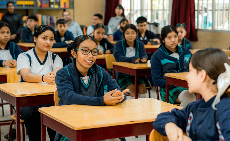  Young adolescents wearing navy blue uniforms are seated at school desks in a classroom