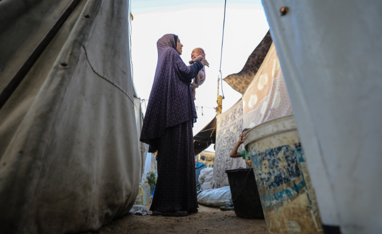 Inas plays with her newborn baby between tents at a displacement camp