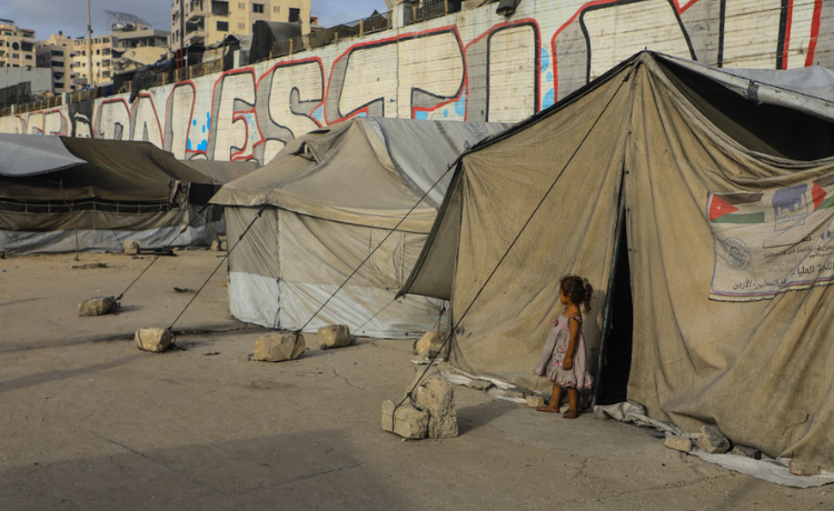 A girl stands at the entrance of her family’s tent in a displacement camp