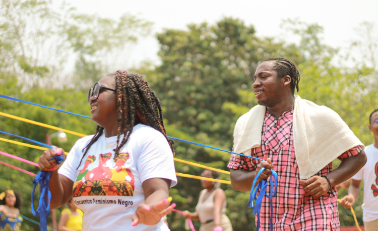 A young woman with glasses and a white t-shirt and a man in a mink checked shirt hold colourful ribbons and smile