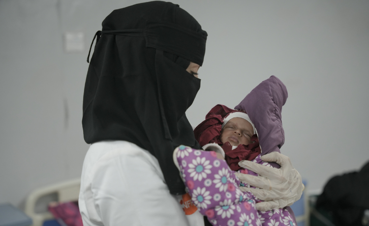 A female health worker holds a newborn baby in a hospita