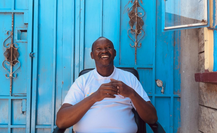 A man smiles broadly in front of bright blue metal doors in the courtyard of the shelter.