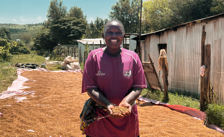 Maryanne stands on a tarp that is being used to dry beans. She cups beans in her hands