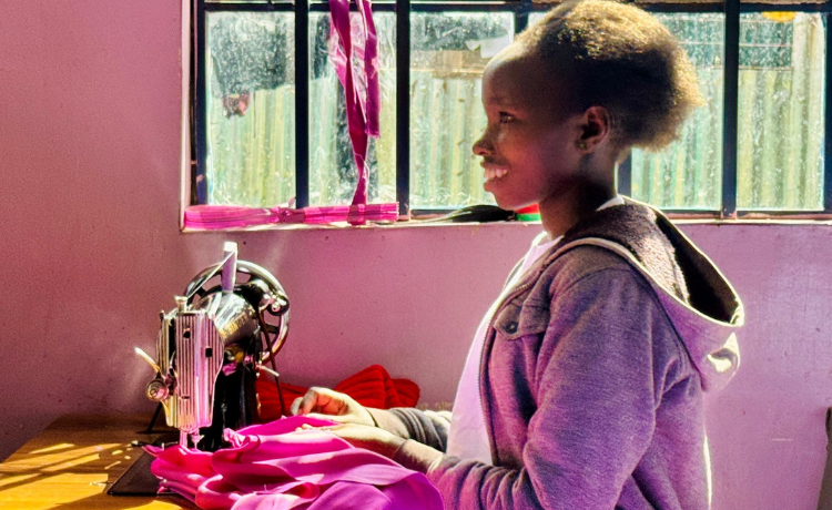 A girl uses a sewing machine to tailor a bright purple cloth.
