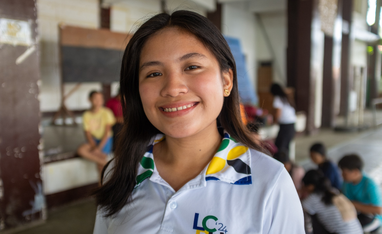 A young woman in a white polo shirt smiles and looks at the camera.