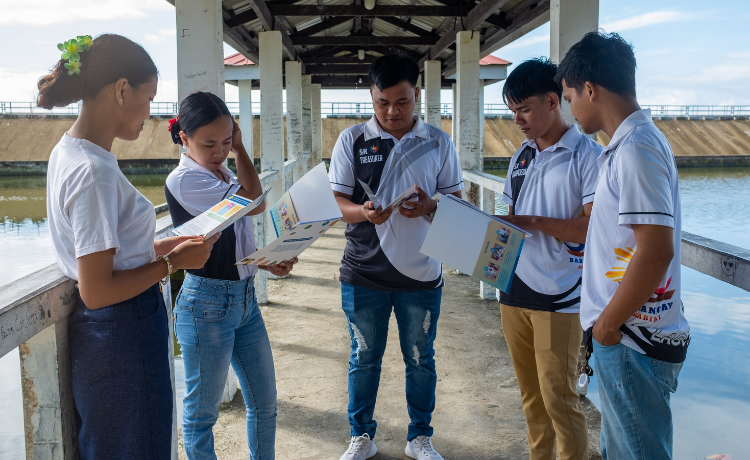 Five young people stand on a bridge holding brochures.