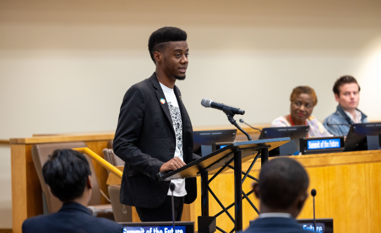 A young man speaks at a podium to an audience at the United Nations.