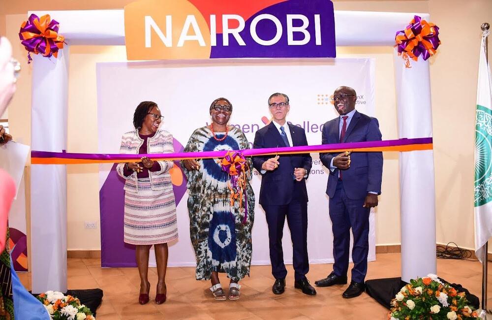 Four people stand before a ribbon with scissors. They smile and pose as they are about to cut the ribbon.