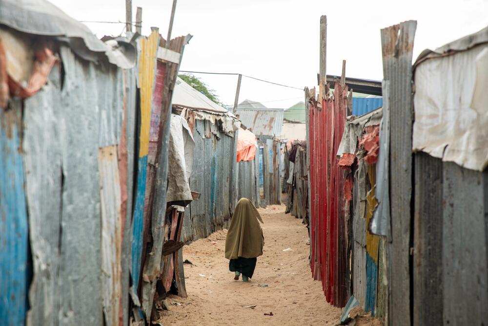 A young girl is seen from behind walking between corrugated iron fronts of temporary homes in a camp for displaced people