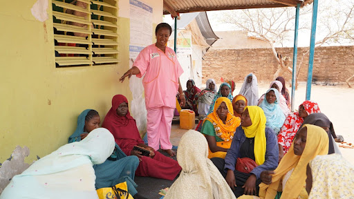 UNFPA Chad/Joel Tchocké [Alt text: A midwife in a pink uniform speaks to a crowd of seated women outside a health centre.