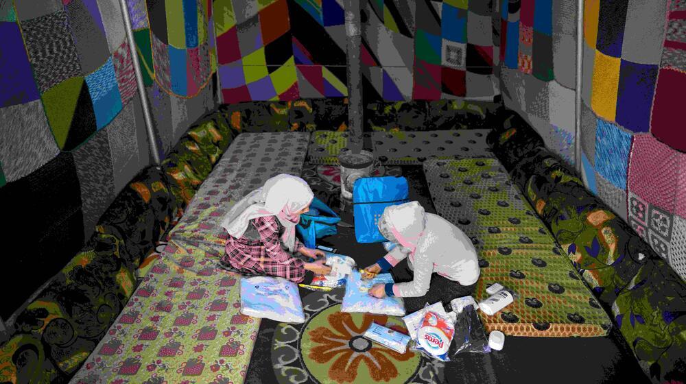 Two young women sit on the floor and look at the contents of their dignity kits - bags with essential hygiene supplies.