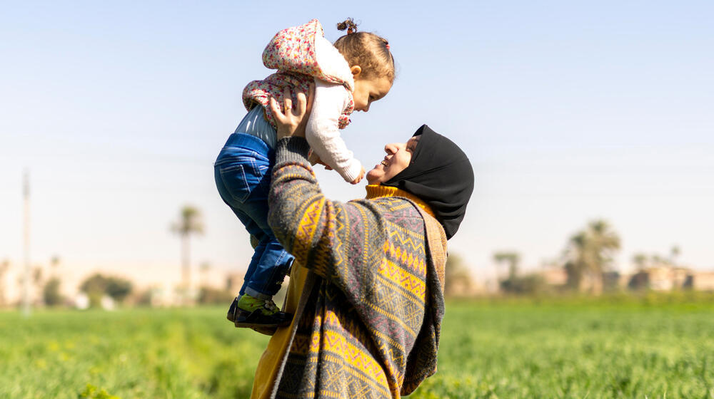 Woman happily holds a smiling child in the air.