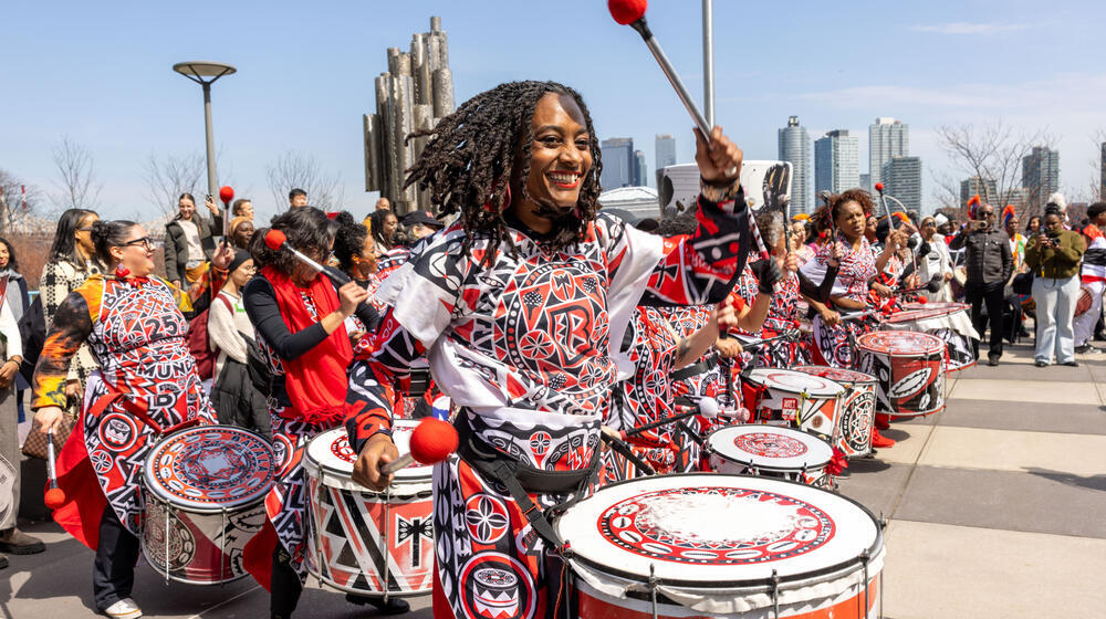 A group of drummers adorned in vibrant clothing are drumming at the UN Headquarters in New York.