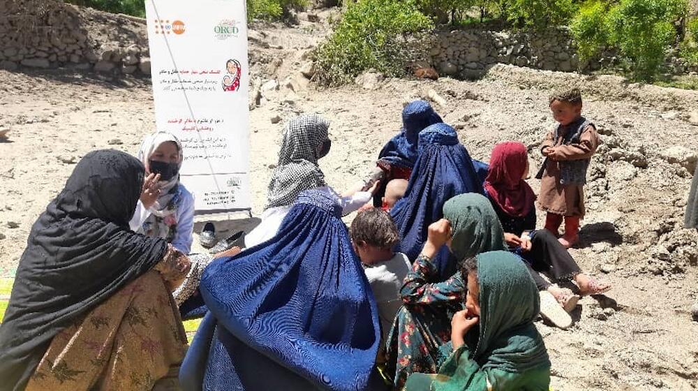 A group of women and children sit talking outside on rocky ground