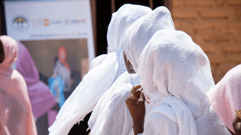 Women in white headscarves are seen from behind, looking towards a large sign with a woman and a UNFPA logo on it