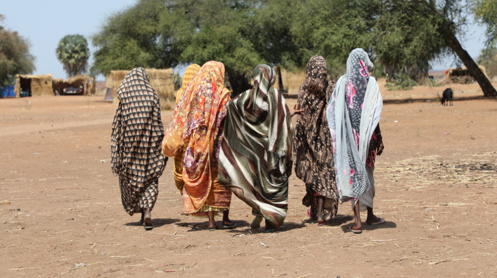Six women wearing long robes are seen walking away towards an open space with a large tree