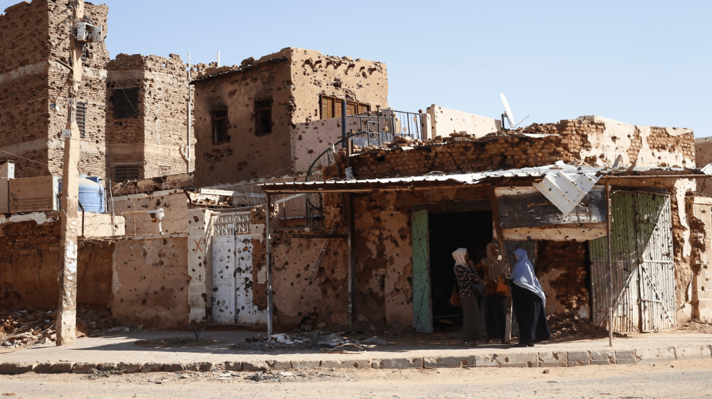 Three women can be seen huddled in the shade of bullet-ridden buildings