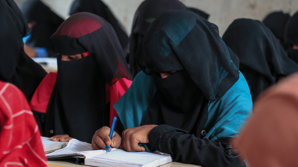  Young girls in black veils write in school books as they sit at desks