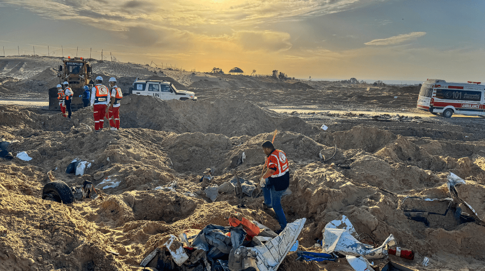 Medical workers, a UN vehicle and an ambulance are seen amid dug up dirt and debris against a setting sun