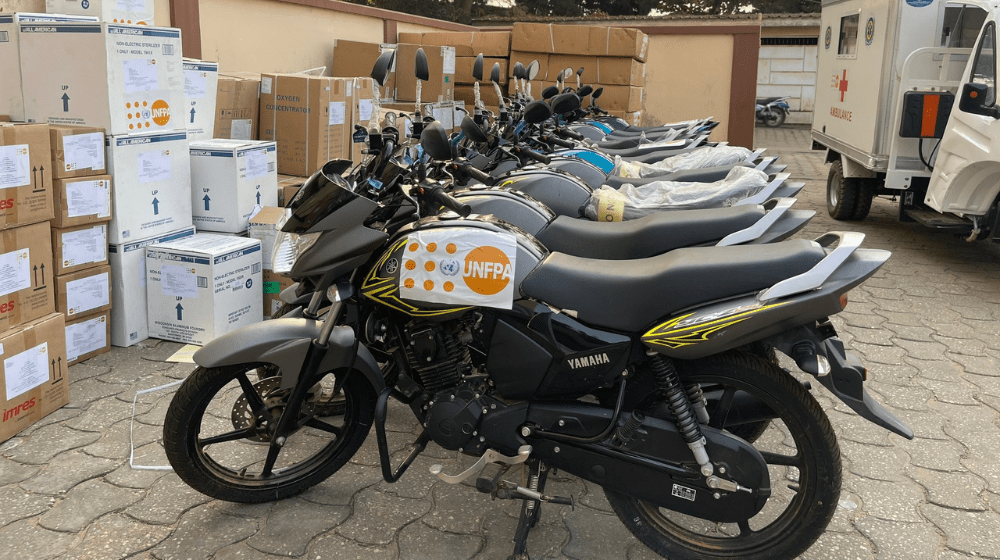 Une dizaine de motos portant le logo de l’UNFPA sont garées en rang, à côté de colis de dons de fournitures de l’UNFPA, dans la cour d’un établissement de santé