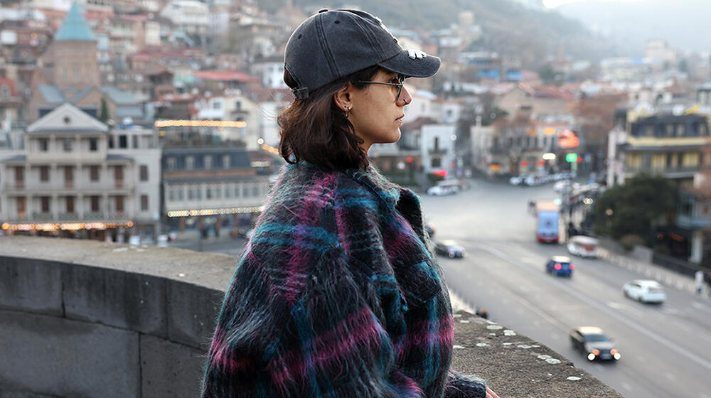 A young woman stands looking over a wall into a city scene.