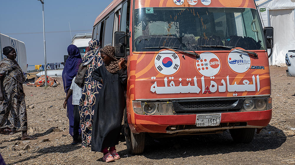 Une jeune fille s’appuie contre un bus orange orné de plusieurs logos, dont celui de l’UNFPA.