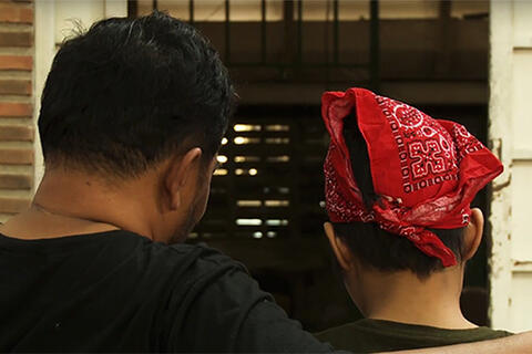 Closeup of adolescent couple; man has his arm over shoulder of woman, and both face away from camera
