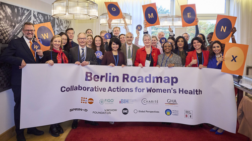 A diverse group of global health leaders holding a banner reading "Berlin Roadmap Collaborative Actions for Women's Health" and individual signs spelling out "WOMEN + X"