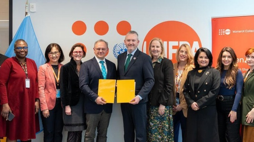 Representatives of UNFPA and FIGO signing a memorandum of understanding at a table in a formal setting, with documents and observers present.